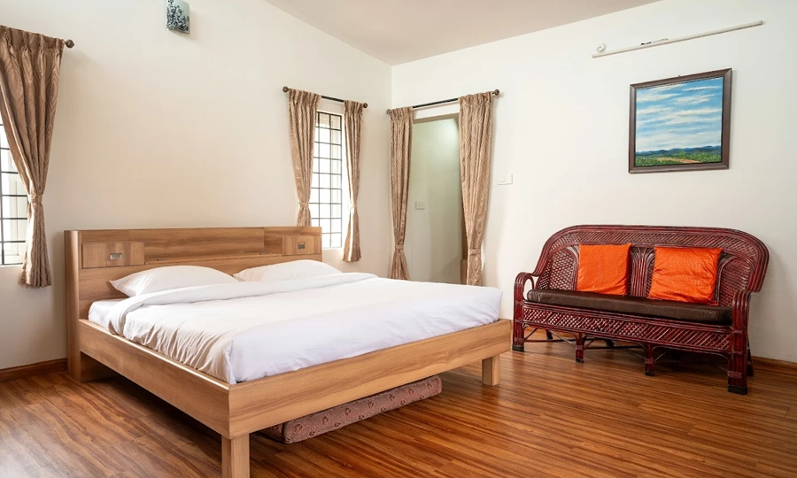 Unwind in a cozy homestay bedroom offering soft linens, fresh breeze, and calm ridge scenery in Kotagiri.